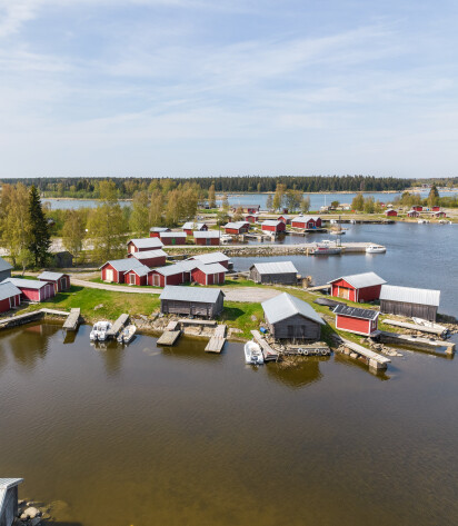 Flygbild över Bergö båthamn med röda båthus och båtar vid bryggor