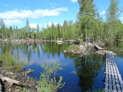 Pieni sisäjärvi, jolla on kiviset rannat ja lankuista rakennettu rantoja myötäilevä ja osittain järven ylittävä polku.