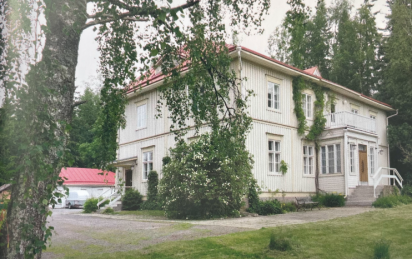 En ljusgrå tvåvånings träbyggnad med rött tack.