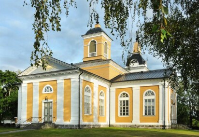Malax kyrka målad i gult och vitt och byggd i ett kors. En klockstapel syns i bakgrunden