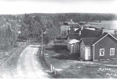 Staket längs grusad byväg och byggnader på landsbygden