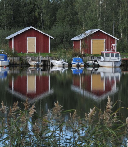 Punaisia venevajoja, joissa keltaiset ovet Maalahden Åminnessä. Venevajojen edessä on veneitä laiturissa.